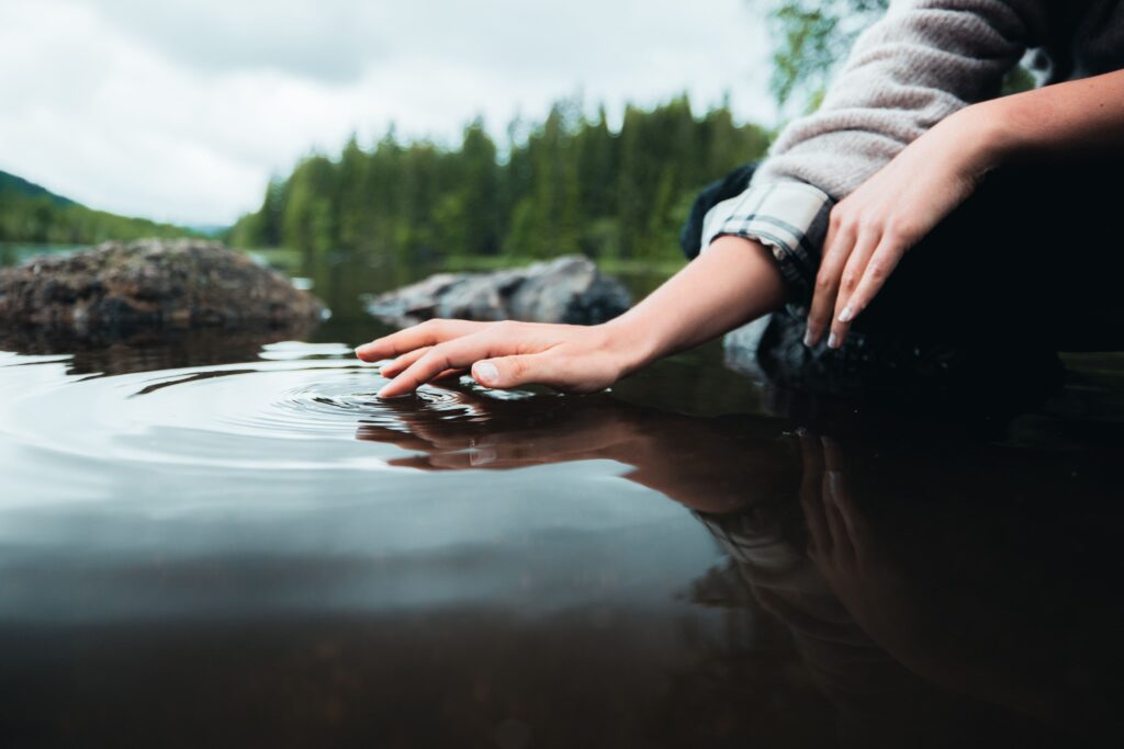 Femme dans la nature qui touche avec sa main de l'eau pour montrer l'importance d'économiser de l'eau avec les produits Hansgrohe