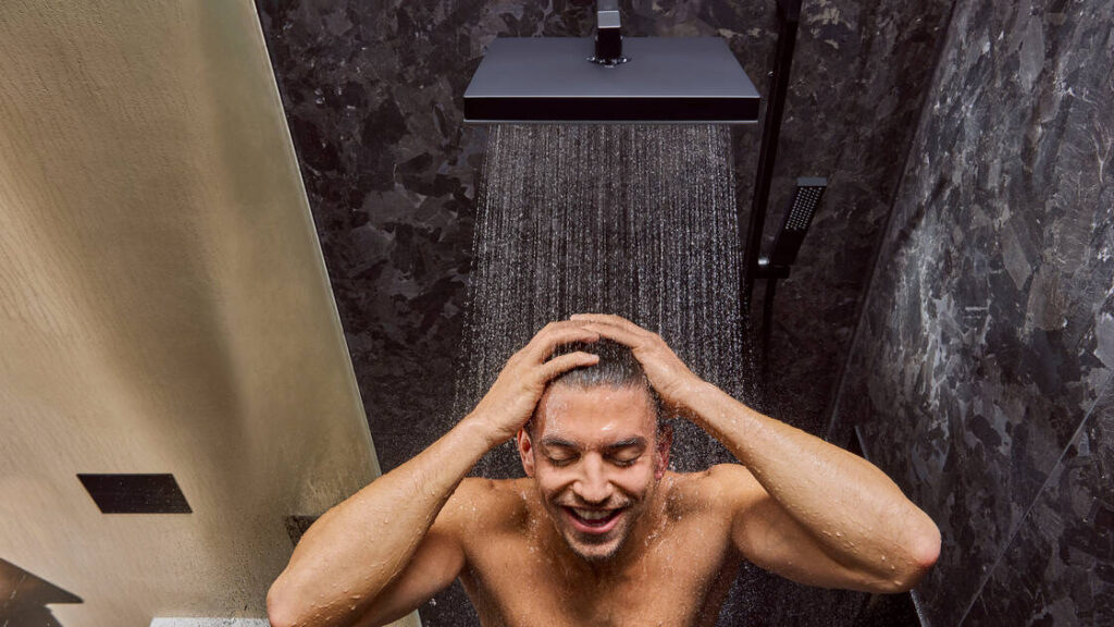 Homme qui prend sa douche avec une douche de tête Pulsify E noir mat de Hansgrohe